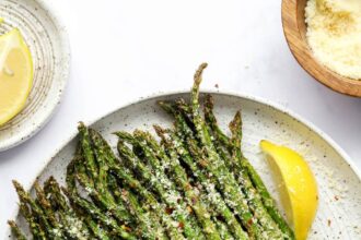 A plate with asparagus and lemon wedges topped with cheese and red pepper flakes.