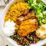 A chicken shawarma bowl with turmeric rice, sliced chicken shawarma, romaine lettuce, Shirazi salad, hummus and Toum.