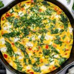 A cooked frittata in a white cast iron skillet topped with fresh parsley. There is a kitchen towel covering the skillet handle.