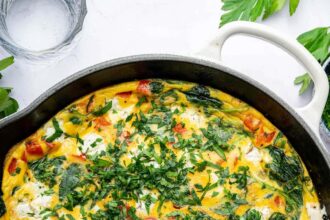 A cooked frittata in a white cast iron skillet topped with fresh parsley. There is a kitchen towel covering the skillet handle.