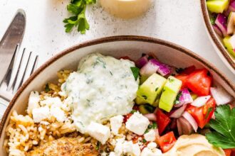 A bowl served with mixed greens, Greek chicken, tzatziki, hummus, cucumber tomato salad and feta cheese.