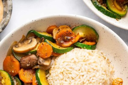 A plate featuring hibachi chicken, brown rice, and sautéed vegetables with a side of creamy dipping sauce.