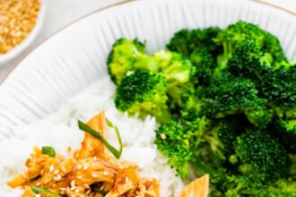 Slow cooker teriyaki chicken served on a plate with white rice and broccoli. The chicken is topped with sesame seeds and green onions.