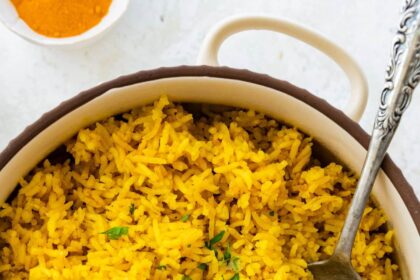 A pot of cooked turmeric rice topped with fresh parsley. There is a silver spoon in the rice.