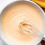 Homemade yum yum sauce in a small ceramic bowl with a silver whisk.